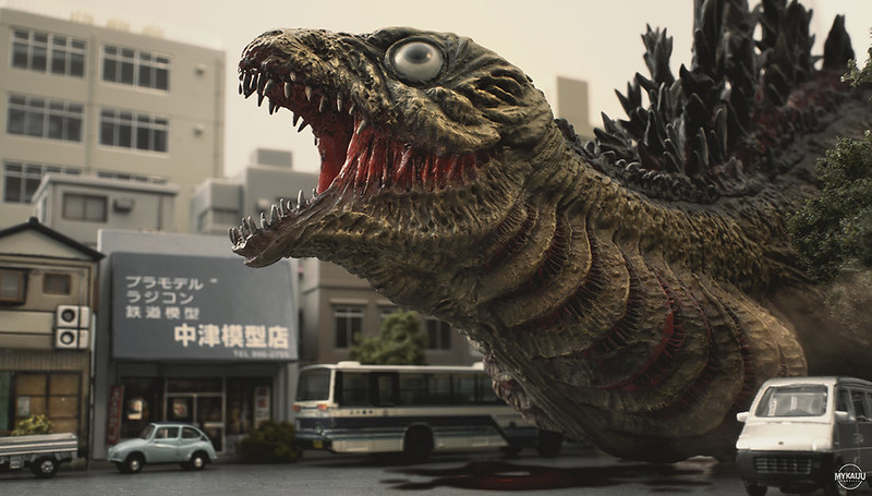 Godzilla in its second form, tadpole-like, with googly eyes, barely able to walk, and leaking fluids, drags itself down a Tokyo street