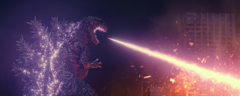 Godzilla in its fourth form, upright and huge, its back covered in glowing spines, shoots a white-hot beam of energy from its mouth, destroying a skyscraper