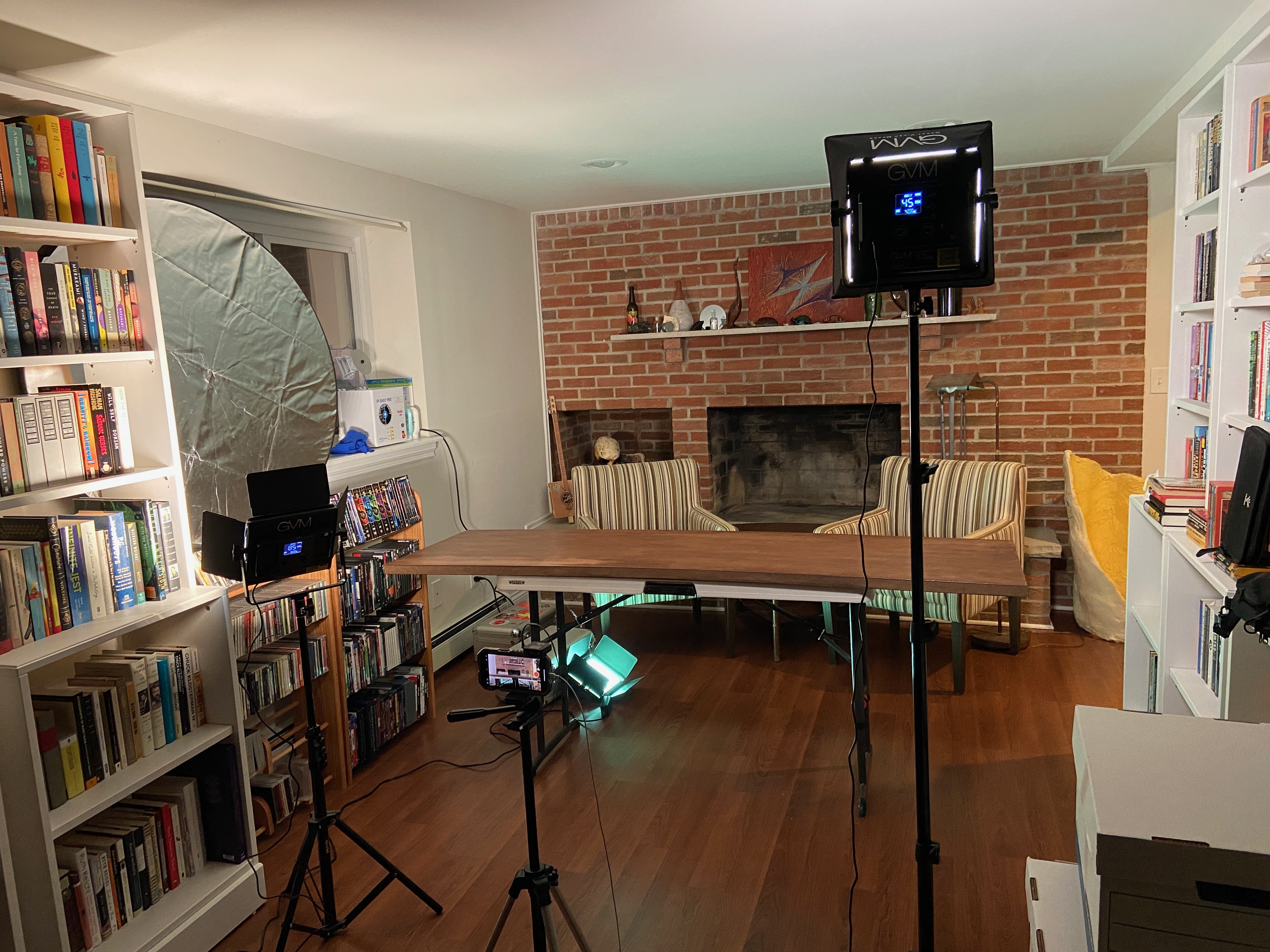 a fireplace with a table in front of it, and tripod-mounted lighting gear