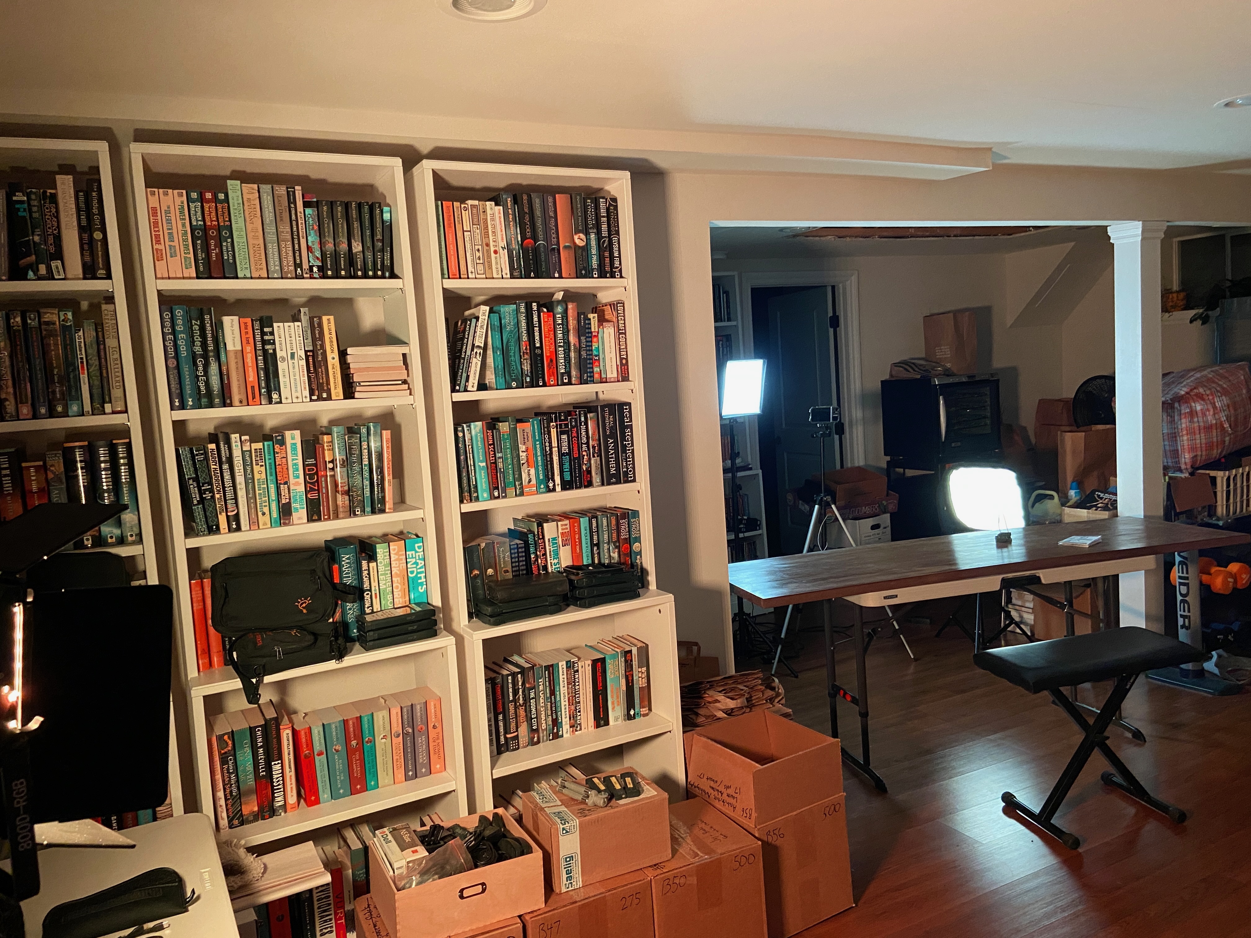 a view of the basement hallway showing a table, an iPhone on a tripod, lighting gear, and boxes