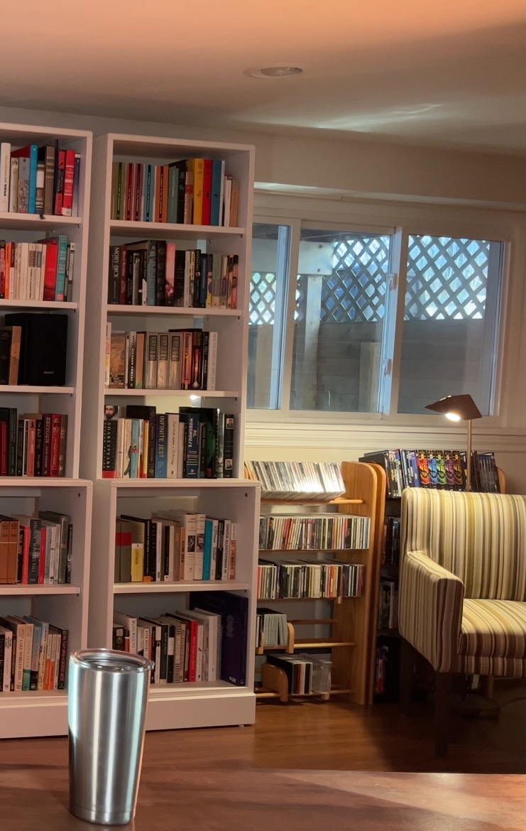 a cropped still frame showing the right side of the basement library, including a window and reading lamp