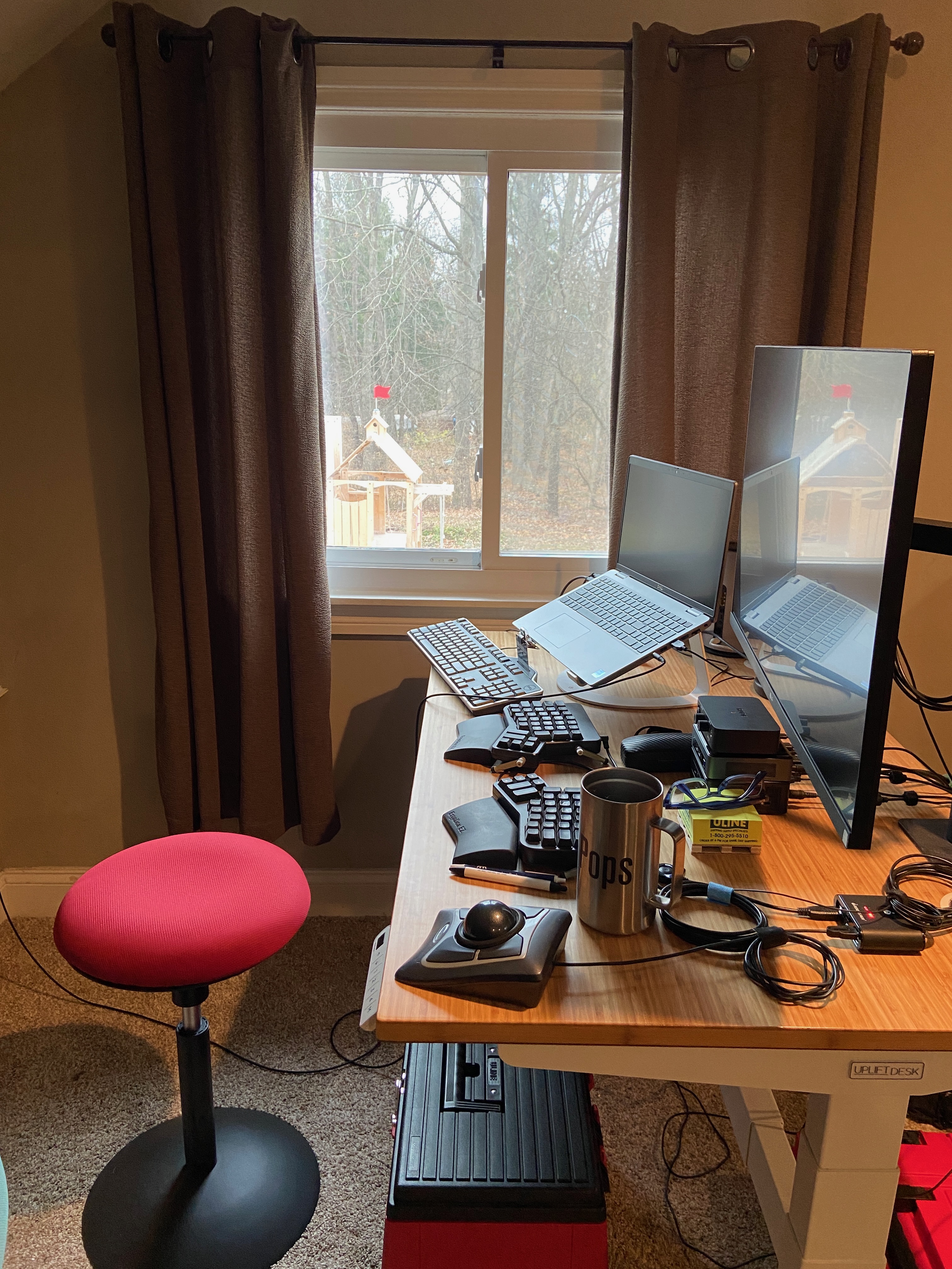 a standing desk holding a large monitor, laptop, and three keyboards